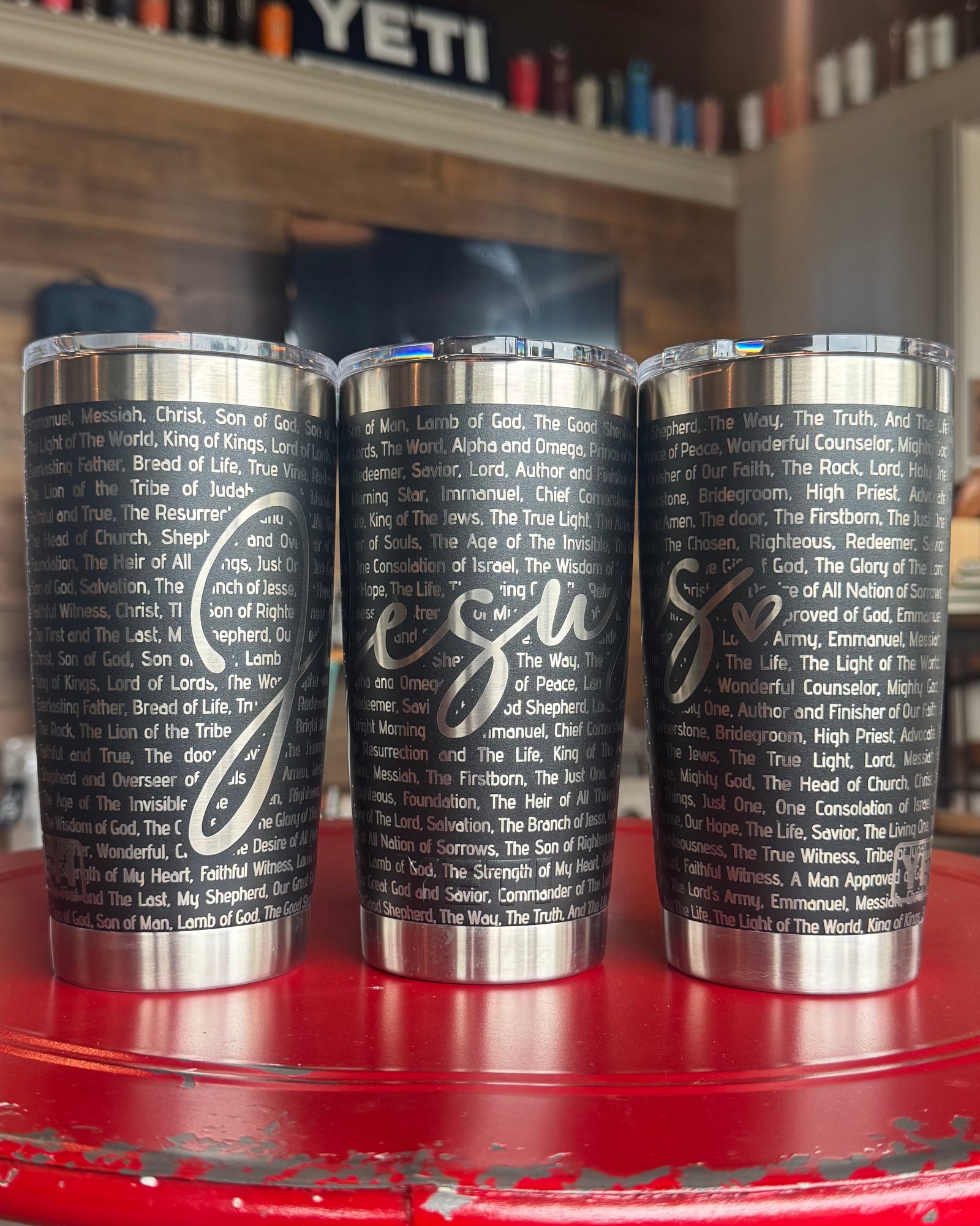 Three stainless steel tumblers with text printed on them, placed on a red surface.